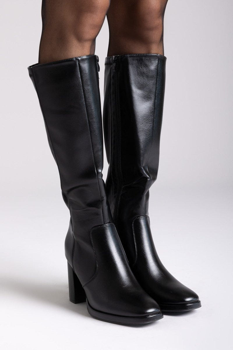 Model legs in black leather knee-high block heel boots with smooth shafts, front view on a light grey background