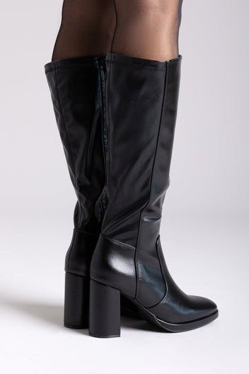 Model legs in black knee-high block heel boots with smooth leather shafts and side zip, front view on a light grey backdrop