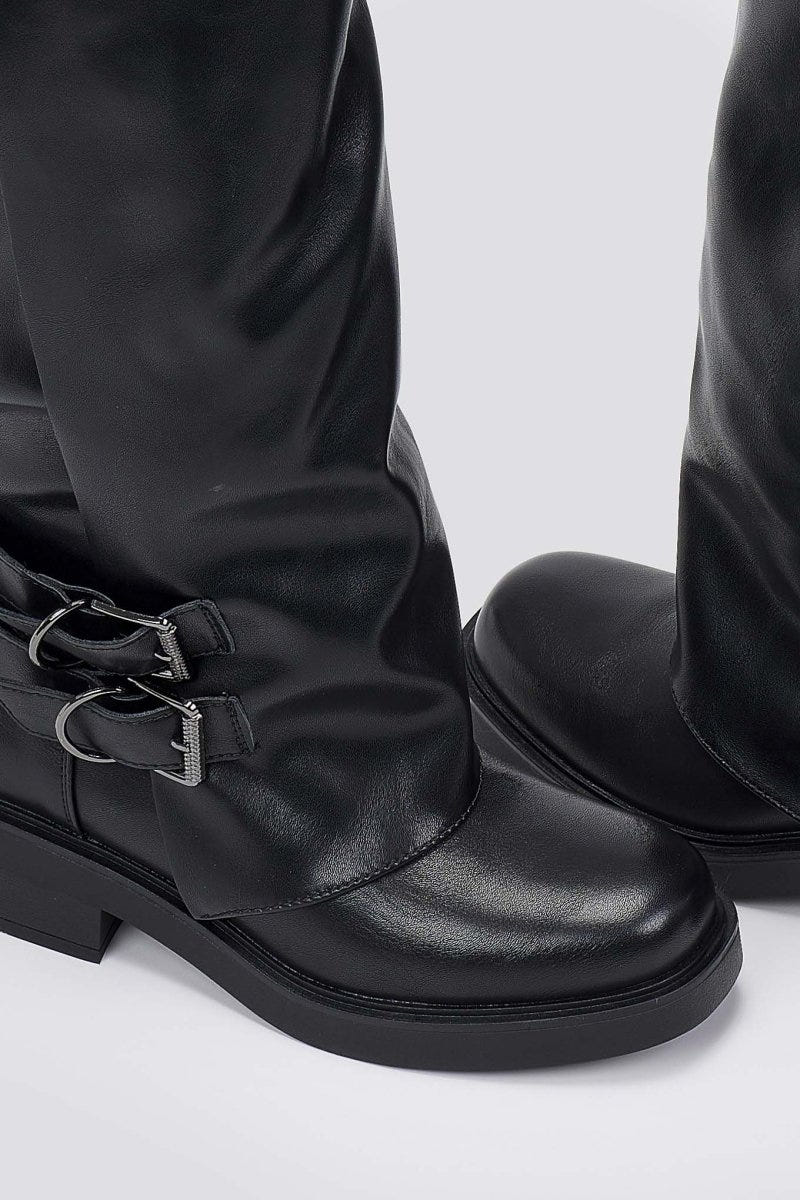 Close-up of black leather boot with a buckle strap and round toe, detail on a light grey background