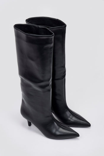Pair of black leather knee-high pointed toe boots with slouchy shafts and kitten heels, angled view on light grey