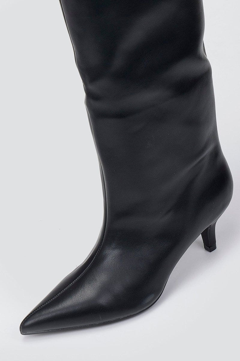 Close-up of black leather pointed toe and kitten heel on a knee-high boot on a light grey background