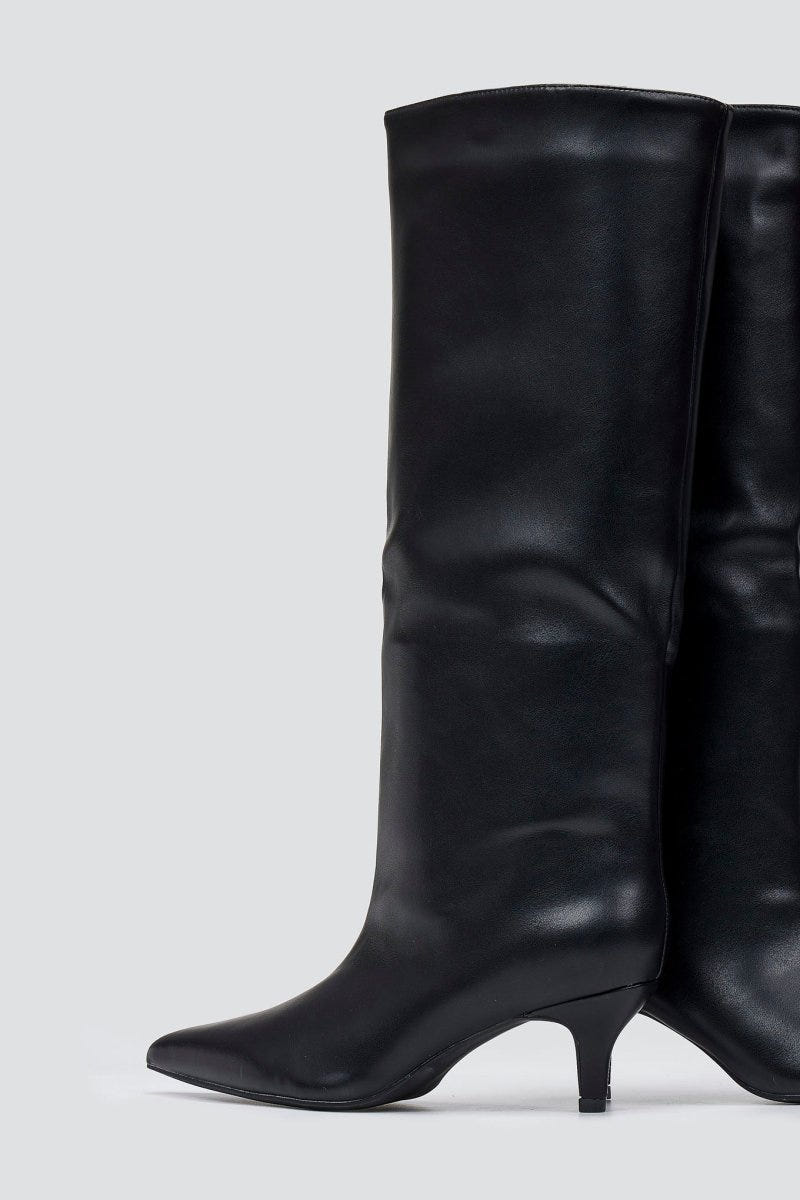 Black leather knee-high pointed toe boot with slouchy shaft and kitten heel, angled side view on a light grey background