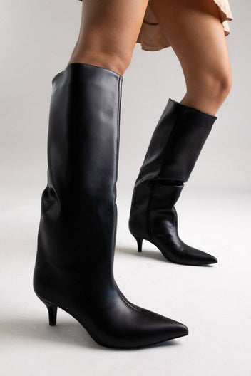 Model legs in black leather pointed toe boots with slouchy shafts and kitten heels, angled view on a light grey backdrop