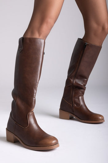 Model legs in brown leather knee-high boots with round toes and tan block heels, angled view on a light grey background
