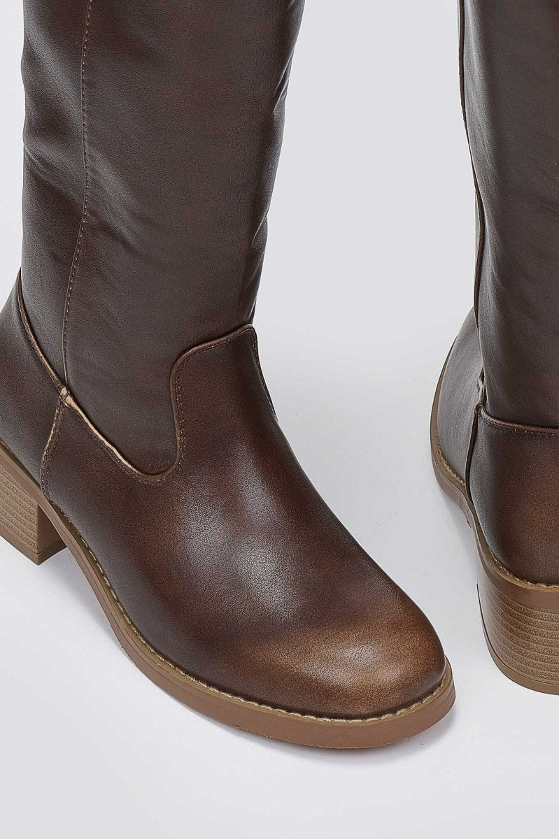 Close-up of brown leather boot shaft and rounded toe with tan block heel on a light grey background