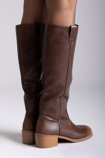 Model legs in brown leather knee-high boots with round toes and tan block heels, front view on a light grey background