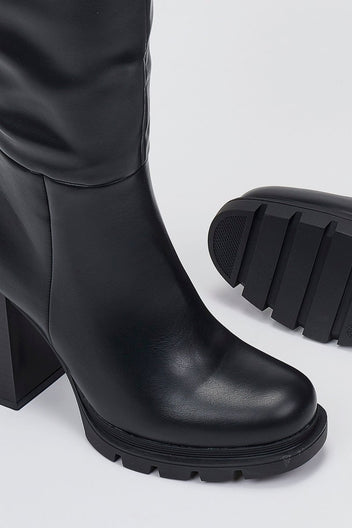 Close-up of black leather boot heel and lug sole edge on a light grey background, showing a chunky block heel