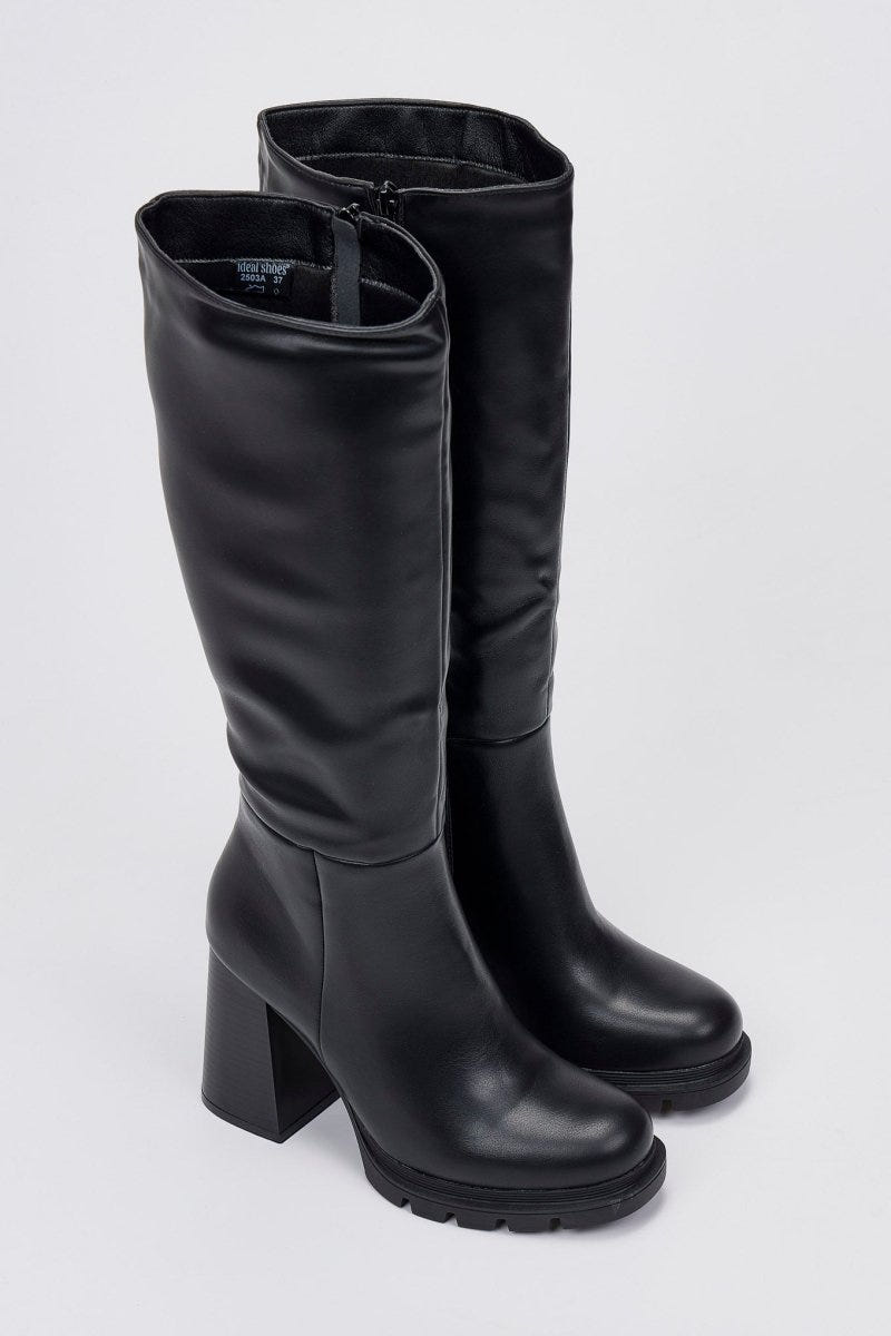 Pair of black leather knee-high boots with lug soles and chunky block heels, angled view on a light grey background