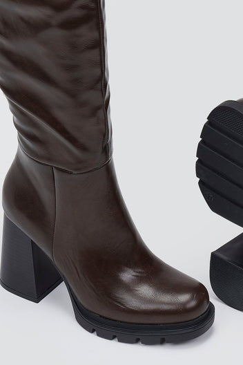 Close-up of dark brown leather platform boot with block heel and lug sole, detail view on light grey background