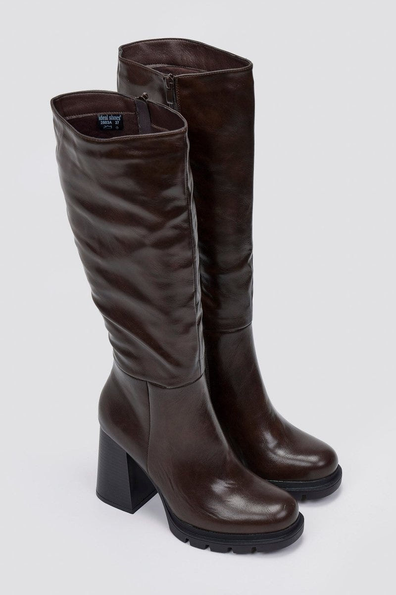 Pair of dark brown knee-high platform block heel boots with lug sole, angled view on light grey background