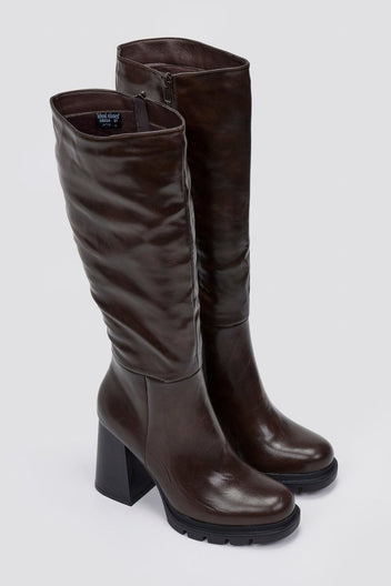 Pair of dark brown knee-high platform block heel boots with lug sole, angled view on light grey background