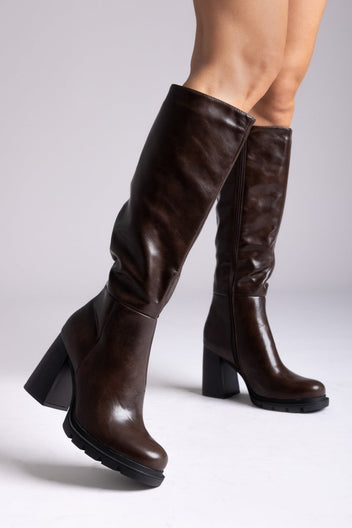 Model legs in dark brown knee-high platform block heel boots with side zip, side view on light grey background
