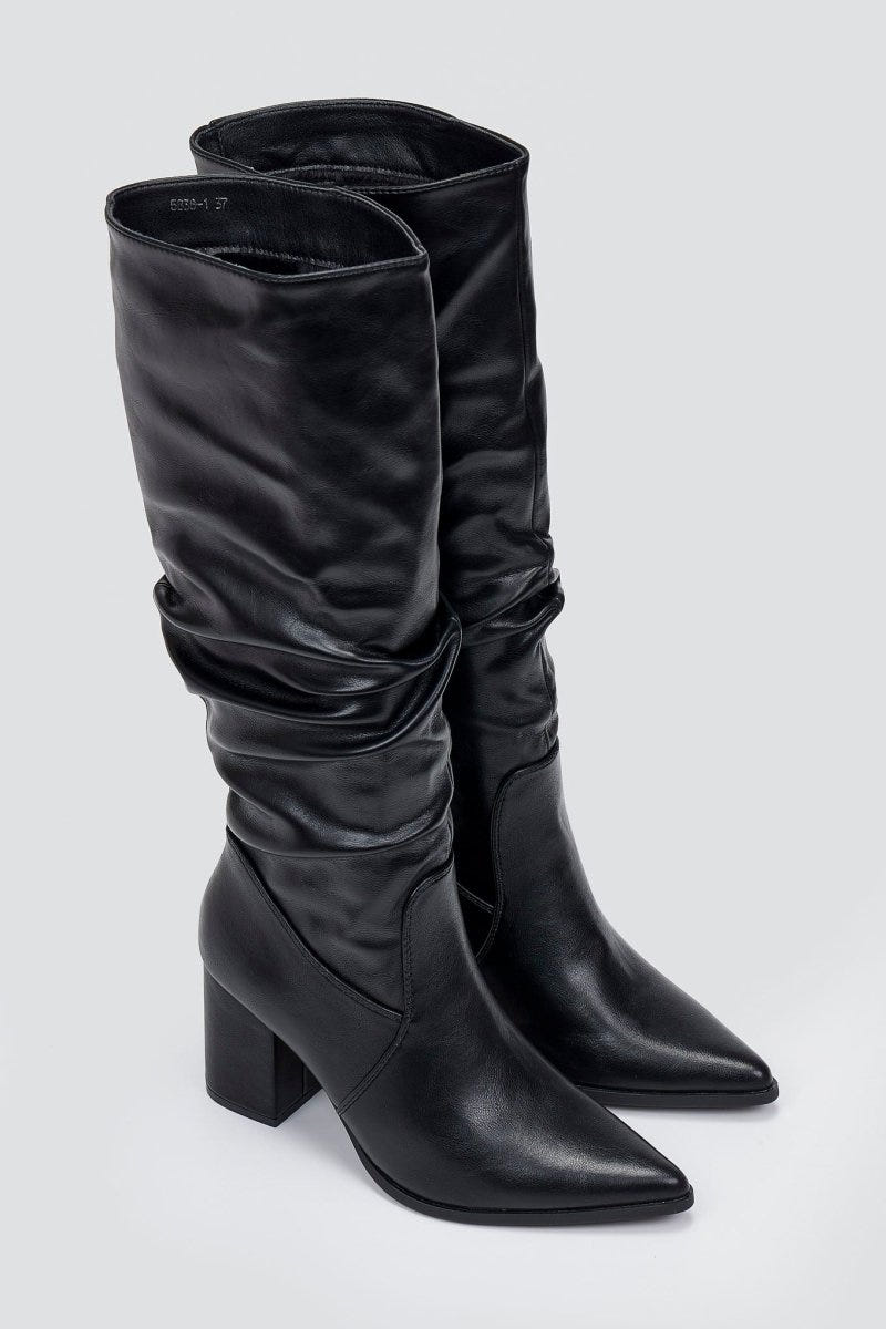 Pair of black knee-high pointed toe block heel boots with ruched slouch shaft, angled view on light grey background