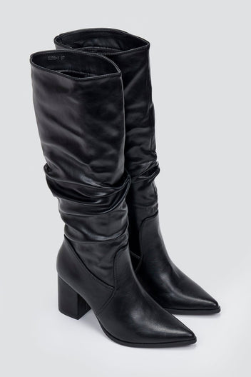 Pair of black knee-high pointed toe block heel boots with ruched slouch shaft, angled view on light grey background