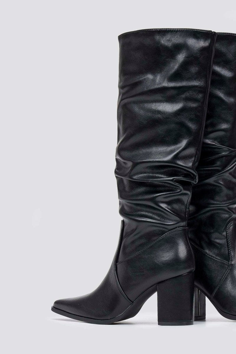 Black knee-high pointed toe block heel boot with ruched slouched shaft, side view on light grey background