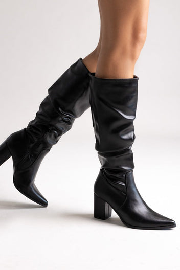 Model legs in black pointed toe ruched knee-high boots with block heel, angled view on light grey background