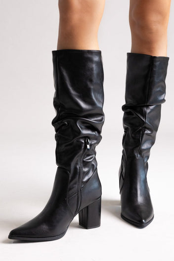 Model legs in black pointed toe ruched knee-high boots with block heel, front view on light grey background