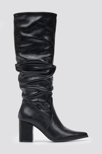 Black knee-high pointed toe block heel boot with slouched shaft and ruched leg, front view on light grey background