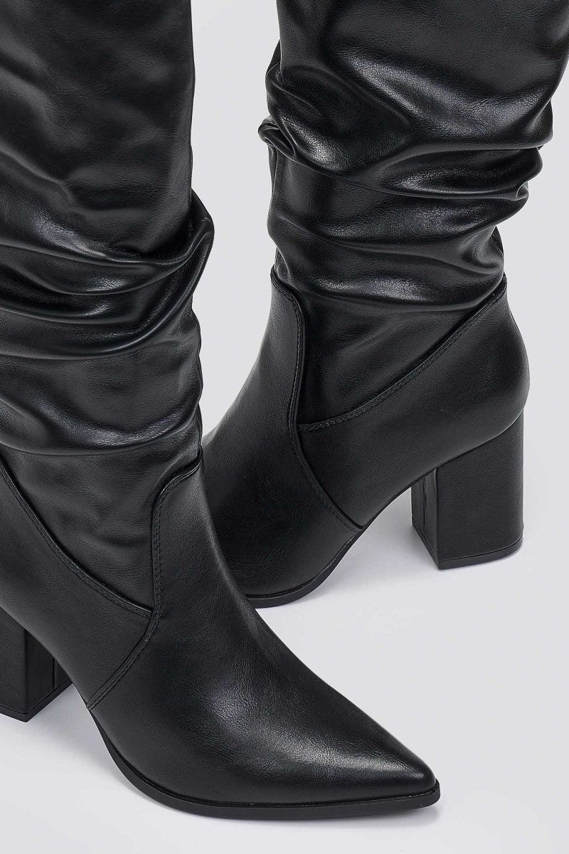 Close-up of black pointed toe boot with ruched slouched shaft and block heel, detail view on light grey background