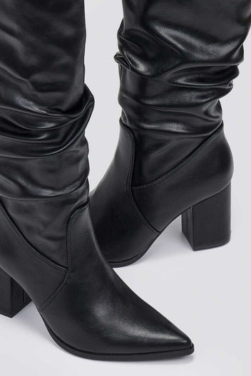 Close-up of black pointed toe boot with ruched slouched shaft and block heel, detail view on light grey background