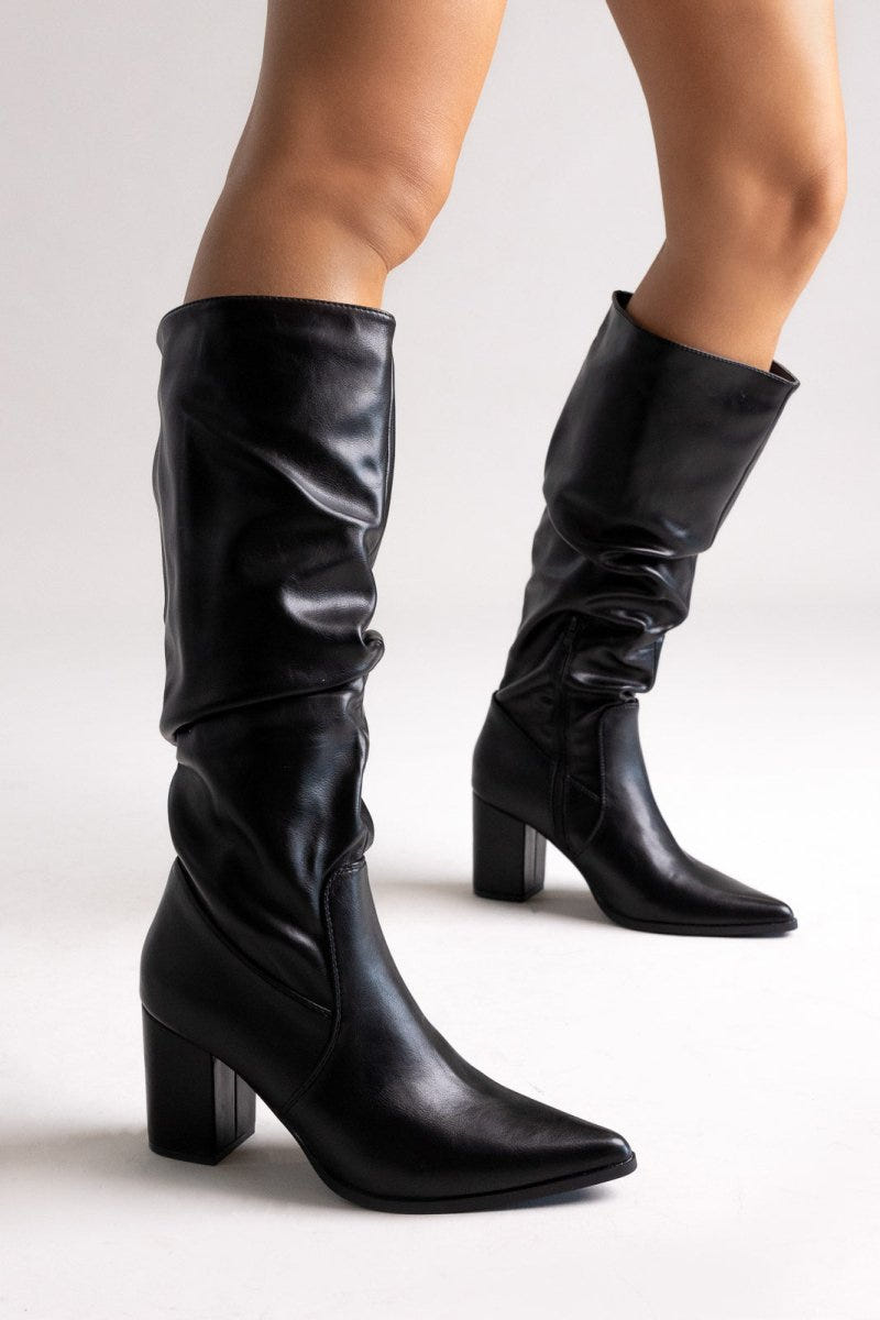 Pair of black pointed toe ruched knee-high boots with block heel, angled view on light grey background