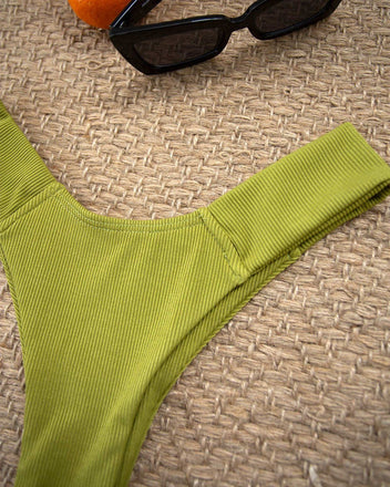 Close-up of lime green textured high-cut bikini bottom laid flat on a woven beige mat with sunglasses at top