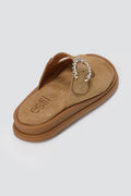 Tan suede slide sandal with decorative silver buckle and chunky sole, angled view on a light grey background