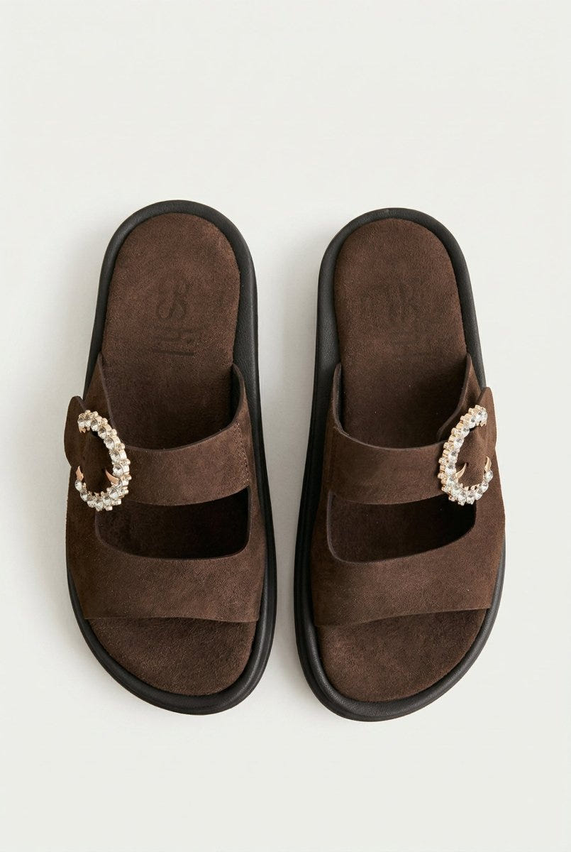Pair of dark brown suede slide sandals with rhinestone buckle and dark chunky sole, overhead view on a light grey background