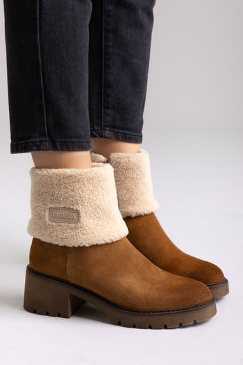 Model legs in tan suede shearling-cuff ankle boots with block heels and dark jeans, angled view on a beige backdrop