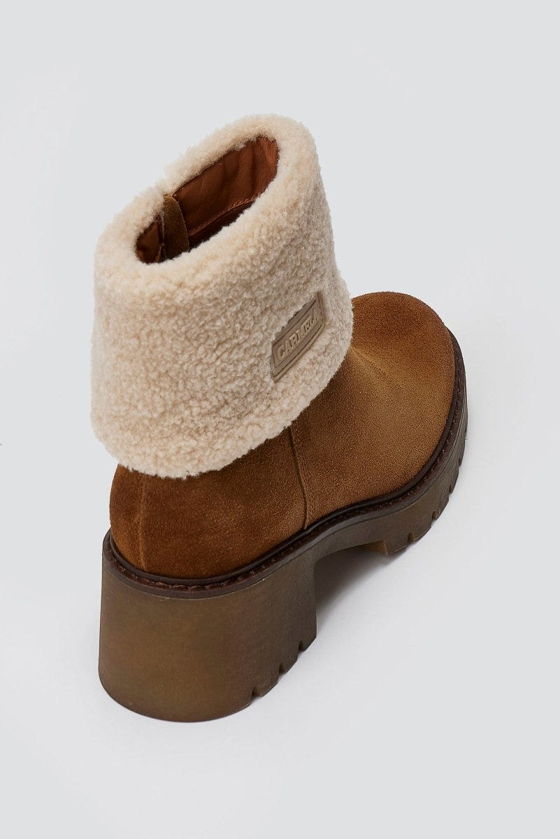 Tan suede shearling-cuff ankle boot with lug sole, top angled view on a light grey background