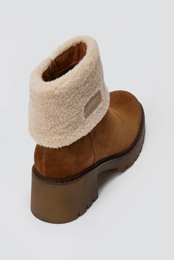 Tan suede shearling-cuff ankle boot with lug sole, top angled view on a light grey background