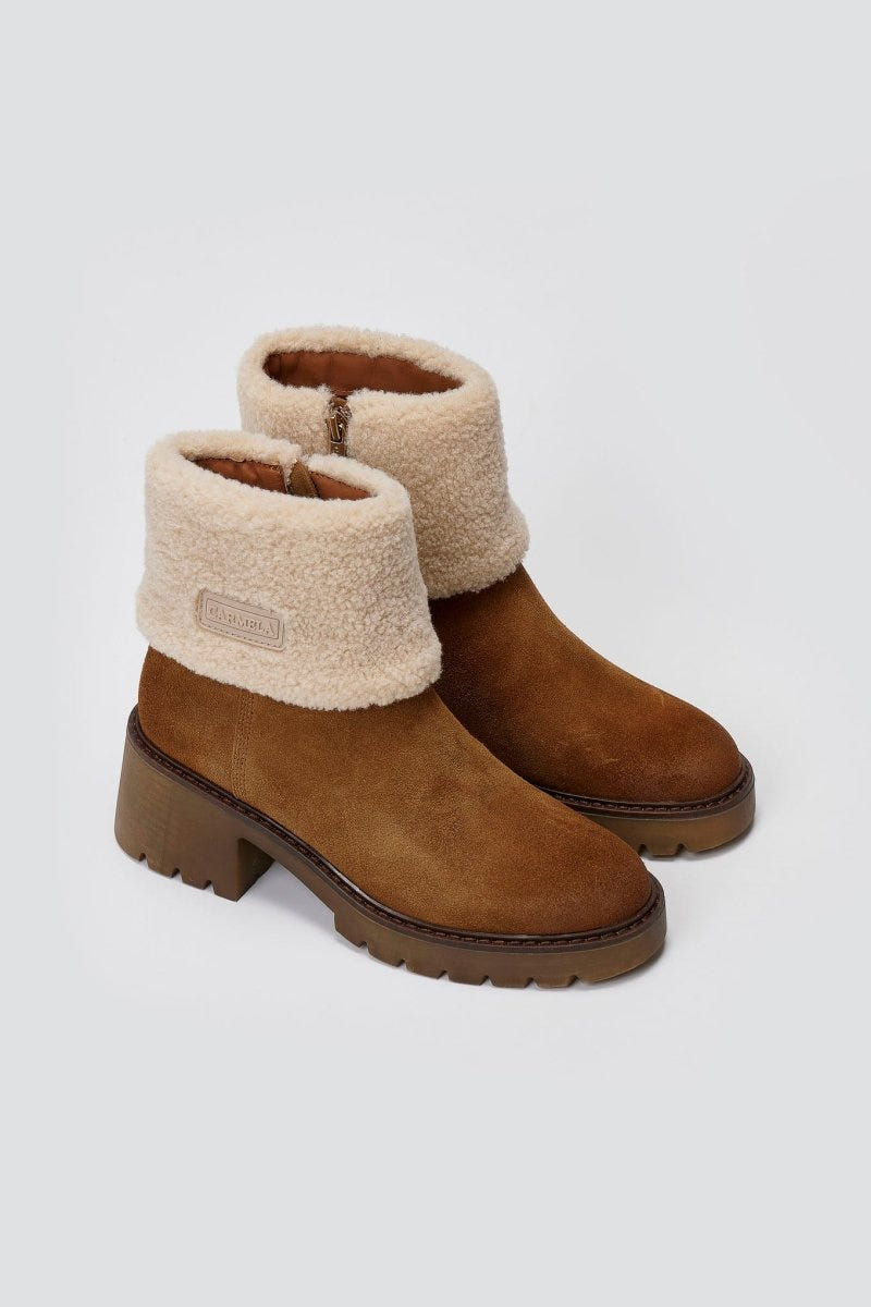 Pair of tan suede shearling-cuff ankle boots with block heels and lug soles, angled view on a light grey background