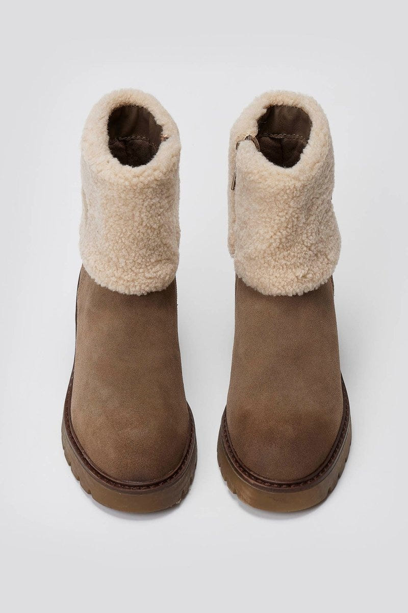 Pair of taupe suede shearling-cuff ankle boots with lug soles, overhead view on a light grey background