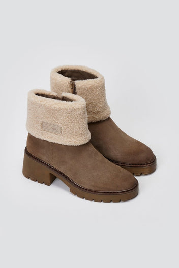 Pair of taupe suede shearling-cuff ankle boots with block heels, angled view on a light grey background