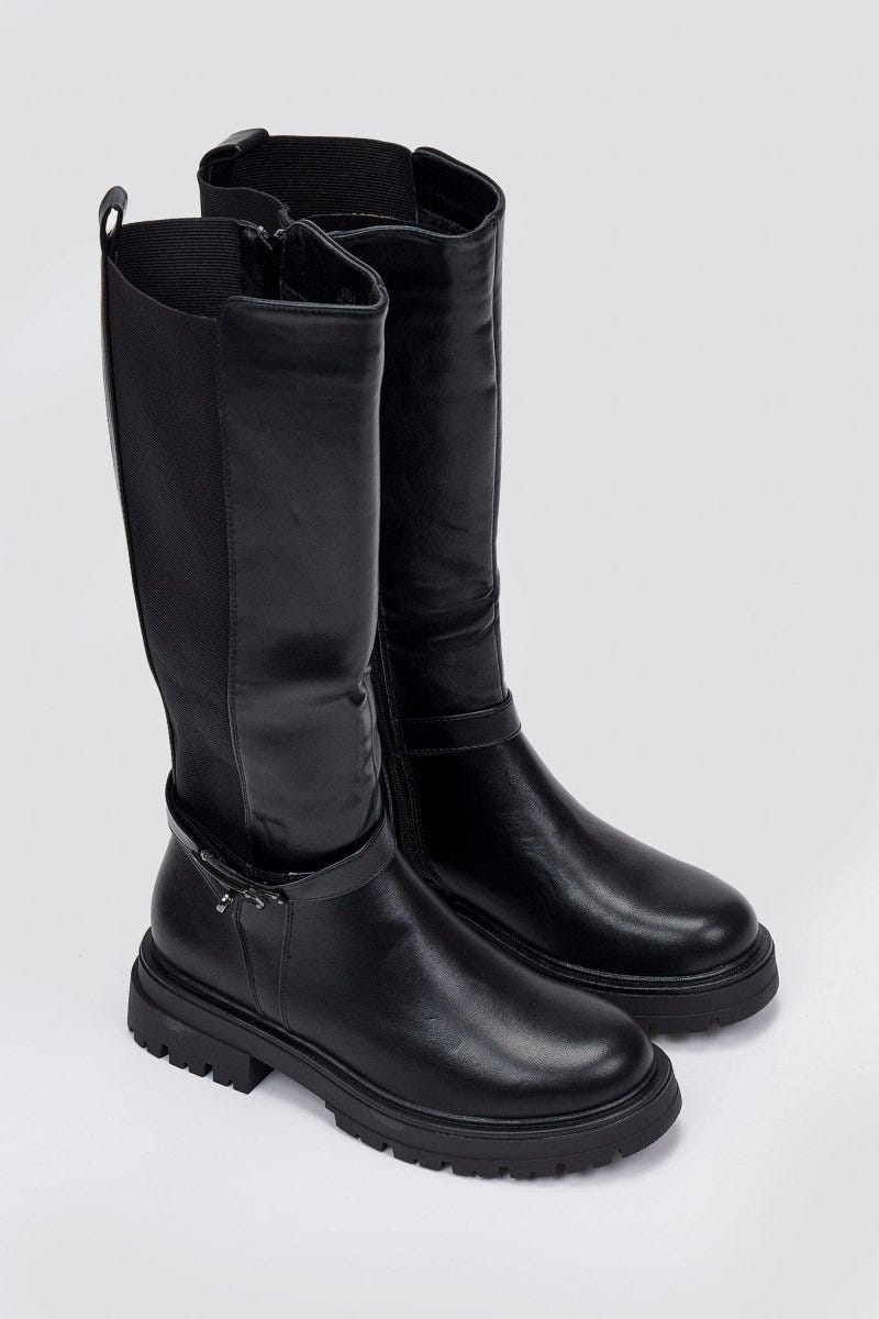 Pair of black leather knee-high lug sole boots with folded cuffs and rounded toes, angled view on a light grey background