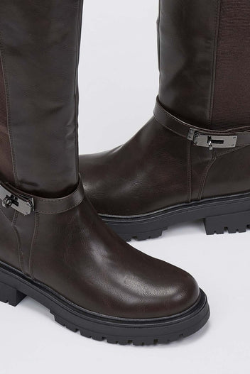 Close-up of dark brown leather lug sole boot with buckle strap and rounded toe on a light grey background