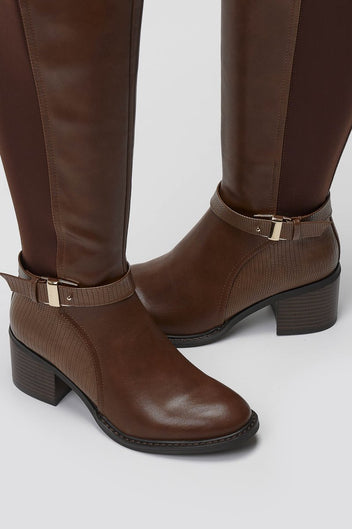 Close-up of tan brown leather block heel boot with buckle strap and rounded toe on a light grey background