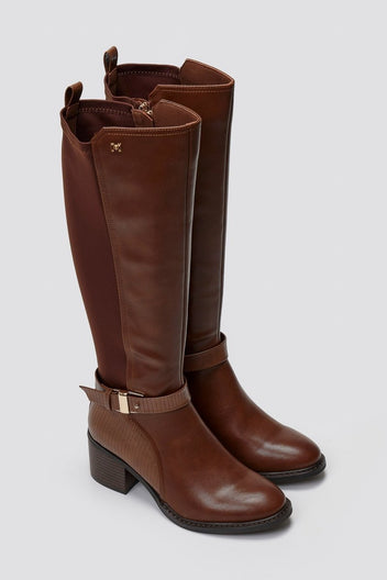 Pair of tan brown leather knee-high block heel boots with gold buckle strap and stretch panel, angled view on light grey