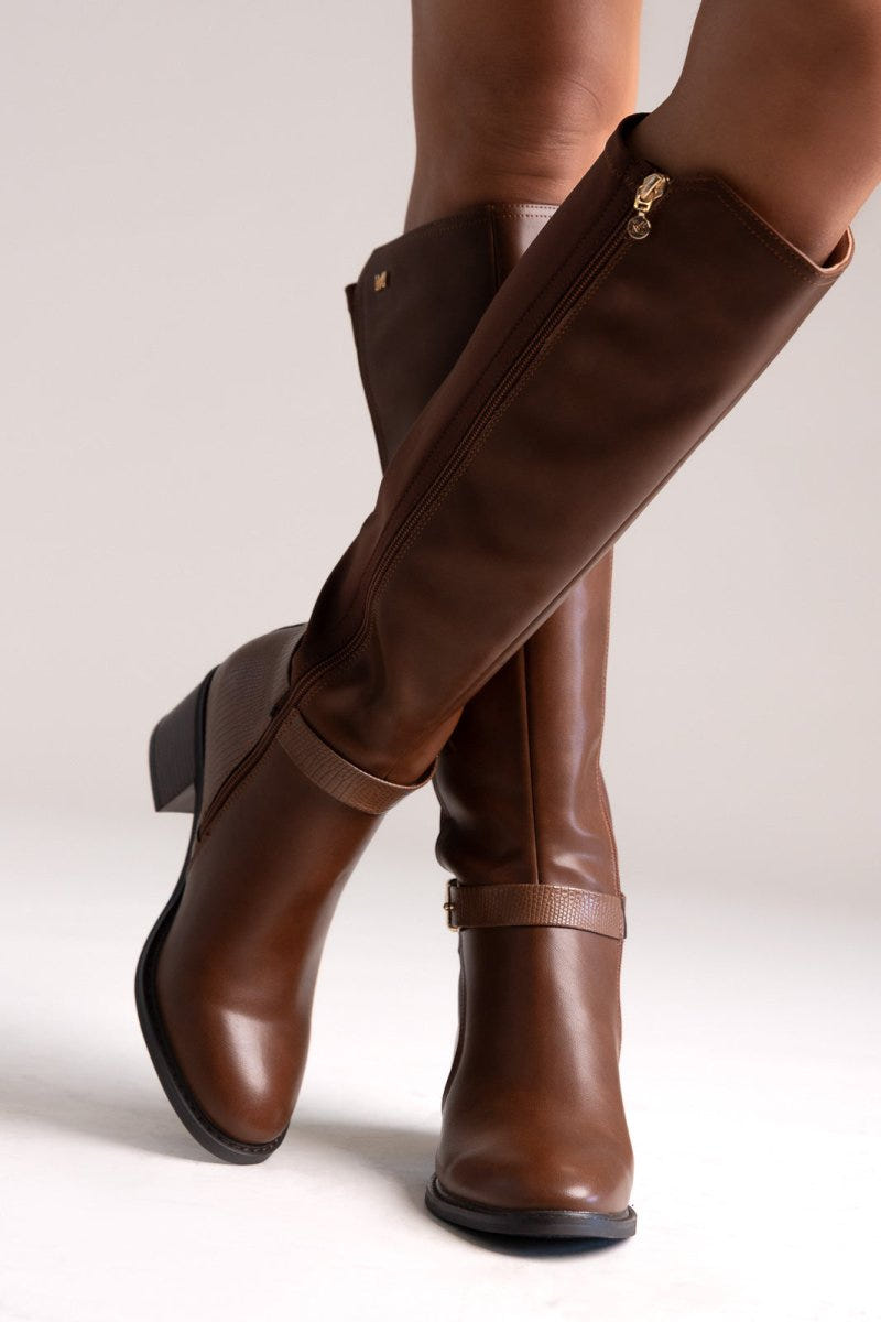 Model legs in tan brown knee-high block heel boots with buckle strap and stretch panel, angled view on a light background