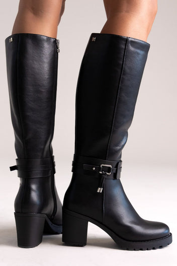Model legs in black leather knee-high block heel boots with buckle strap and side zip, angled view on a light background