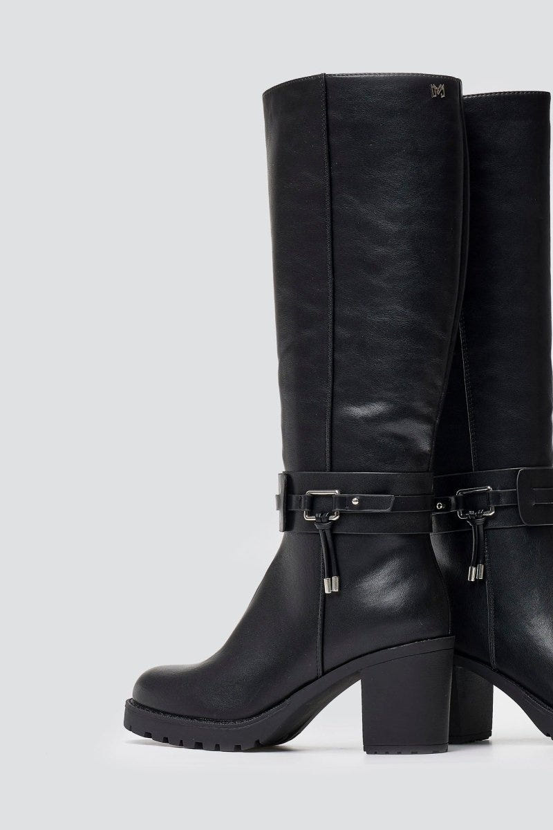 Pair of black leather knee-high block heel boots with gold buckle strap and round toes, angled view on a light grey background