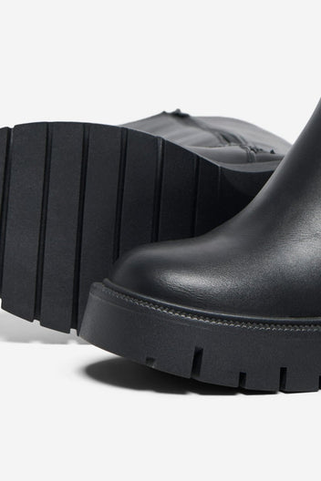 Close-up of black leather boot with chunky lug sole and rounded toe on a light grey background