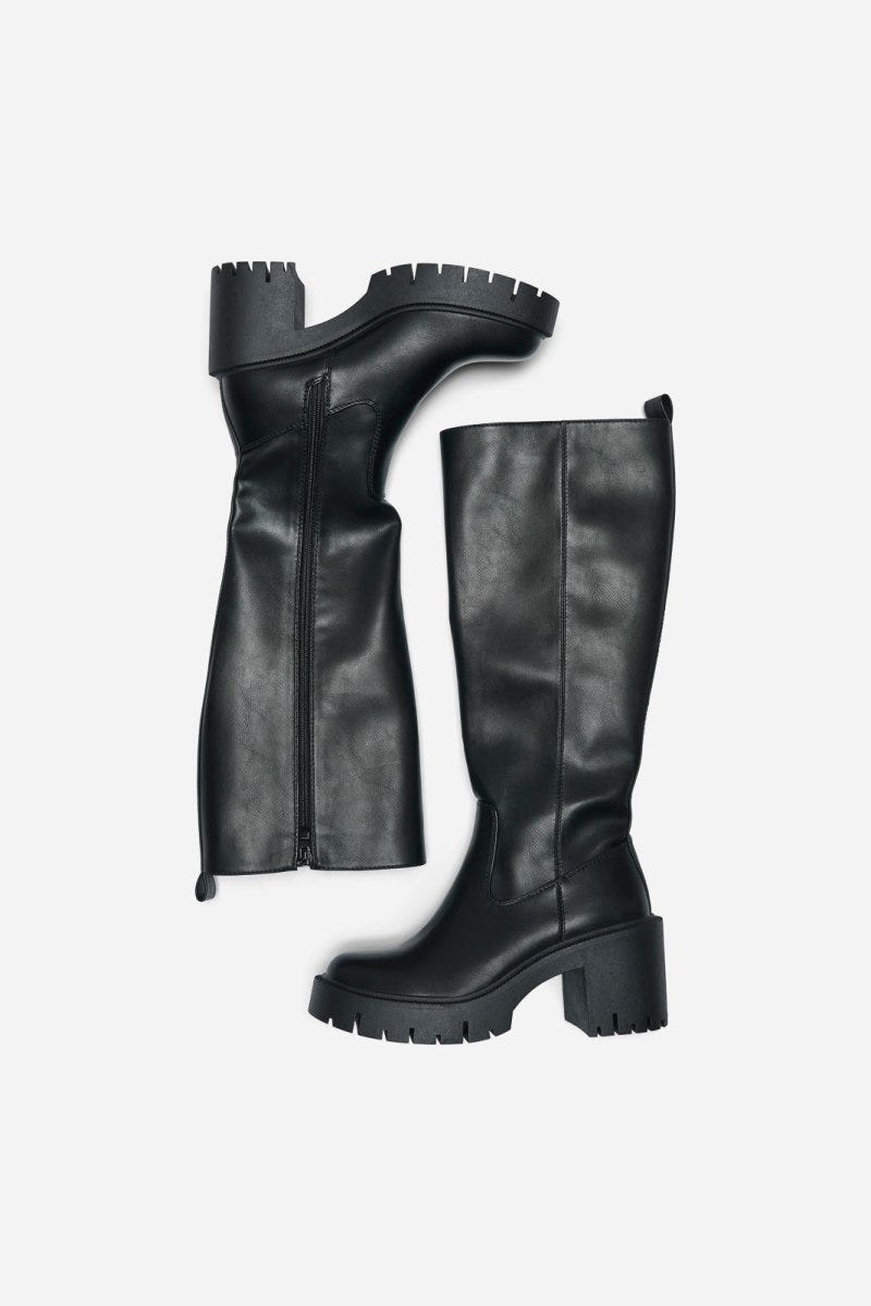 Pair of black leather knee-high boots with chunky lug soles and block heels, overhead angled view on a light background