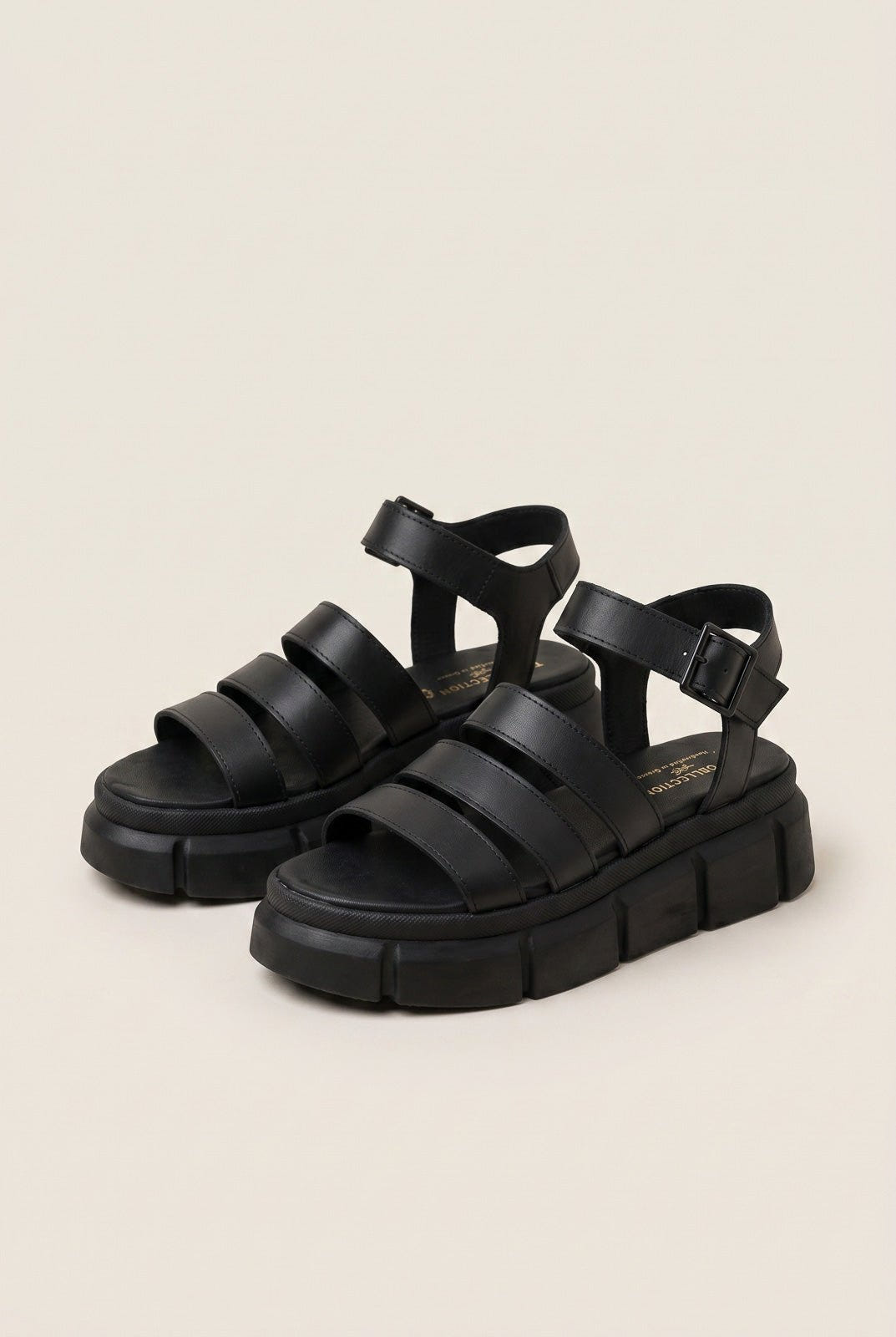 Pair of black chunky platform sandals with wide straps and buckle closure, angled view on a light beige background