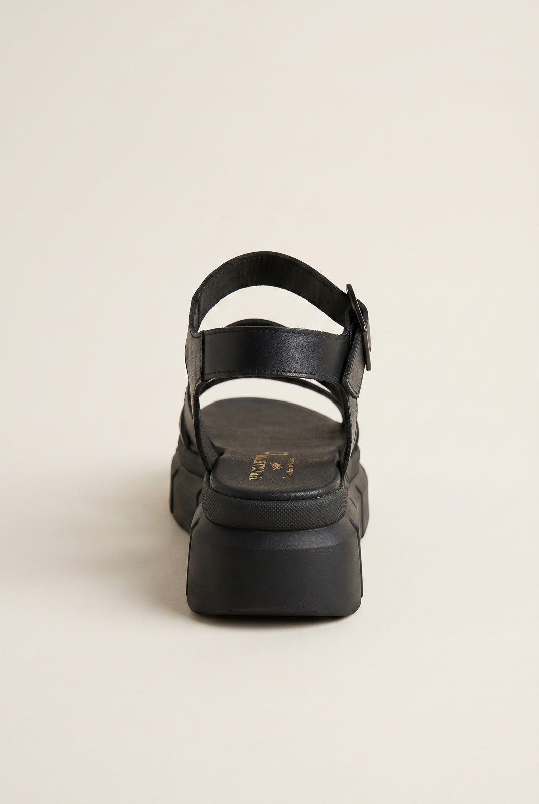 Black chunky platform sandal with ankle strap and buckle, rear view on a light beige background