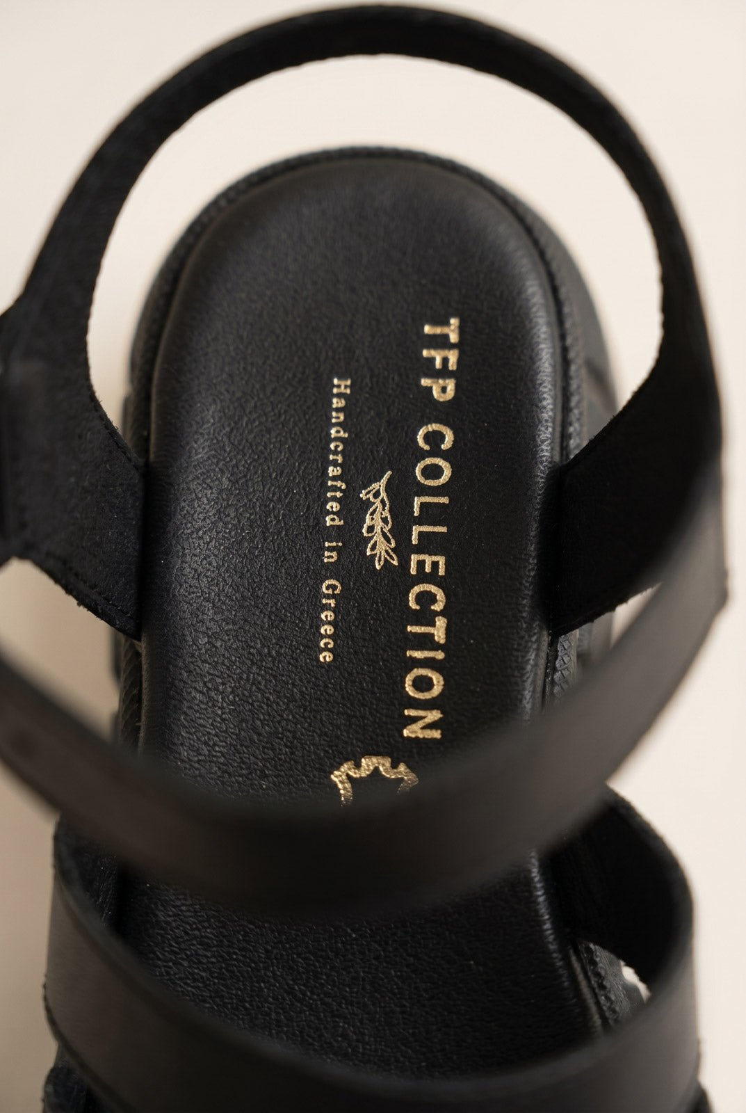 Close-up of black chunky sandal heel strap and dark footbed with a small gold printed mark on a light background