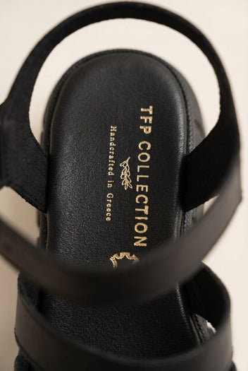 Close-up of black chunky sandal heel strap and dark footbed with a small gold printed mark on a light background