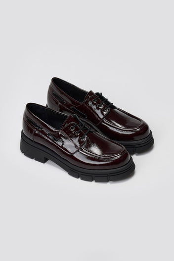 Pair of burgundy patent leather chunky sole lace up shoes, angled view on light grey background