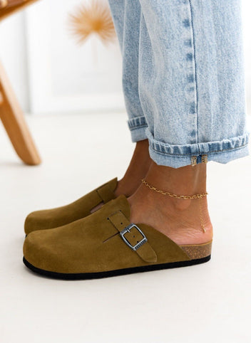 Model foot in olive suede clog with buckle strap and cork footbed in front of rolled light denim jeans