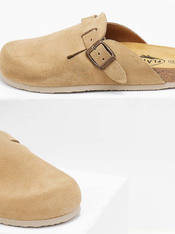 Close-up of beige suede clog toe area and buckle strap resting on a white block with soft shadow